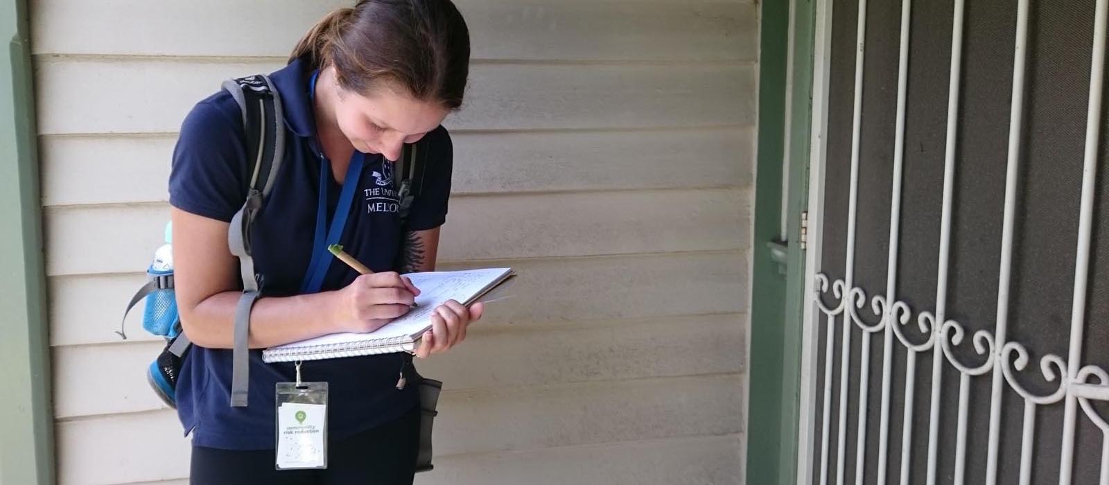 Woman writing on a note pad outside the entrance to a house.